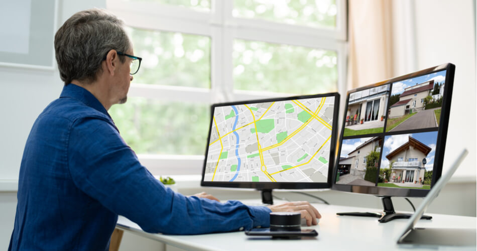 Man looking at computer with two screens of houses and a map