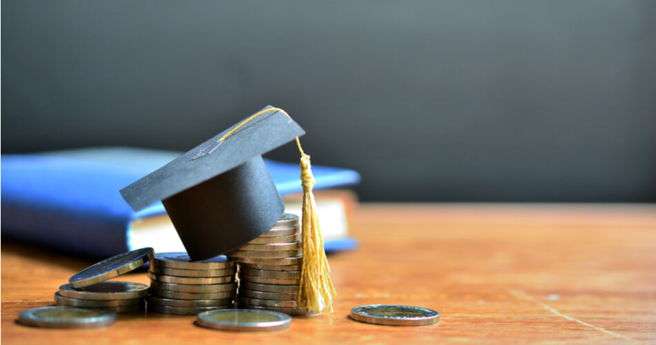 Stacks of coins with graduation cap on top and a blue book in background