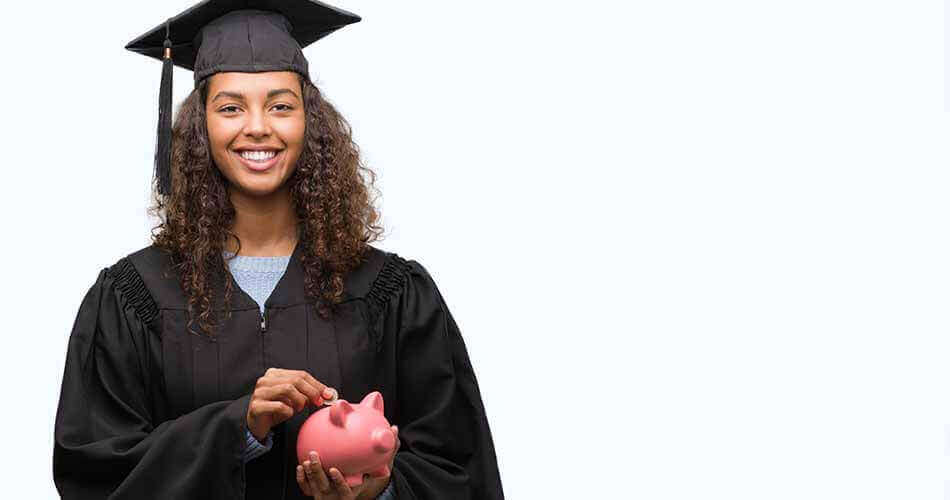 Woman in graduation cap and gown holding a piggy bank