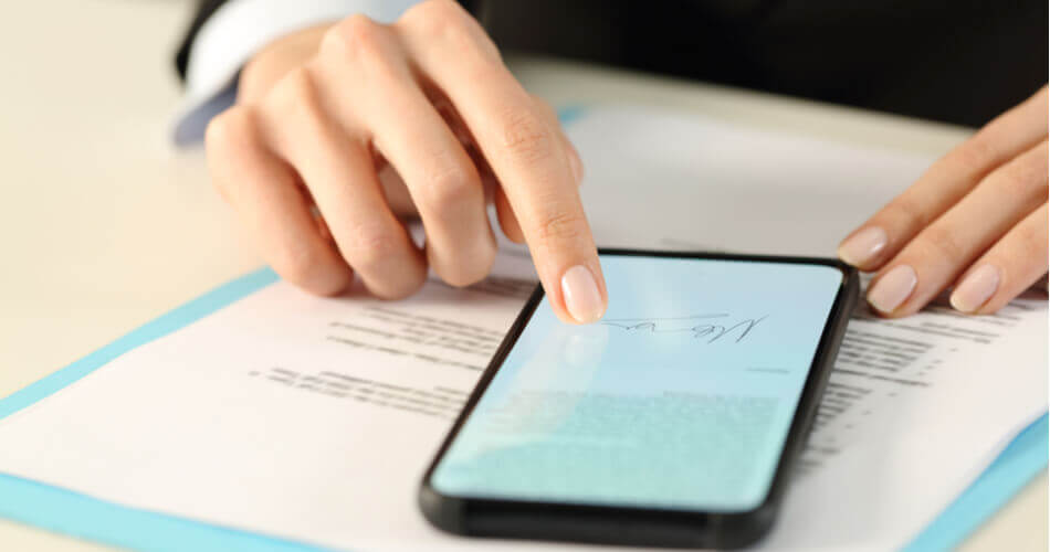 Man signing a document on his phone on top of physical documents
