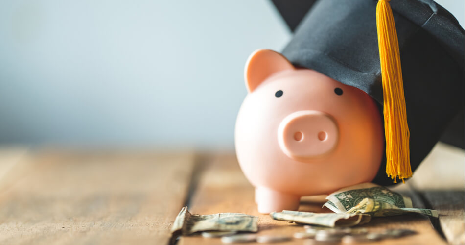 Piggy bank wearing a graduation cap with crumpled dollar bills in front