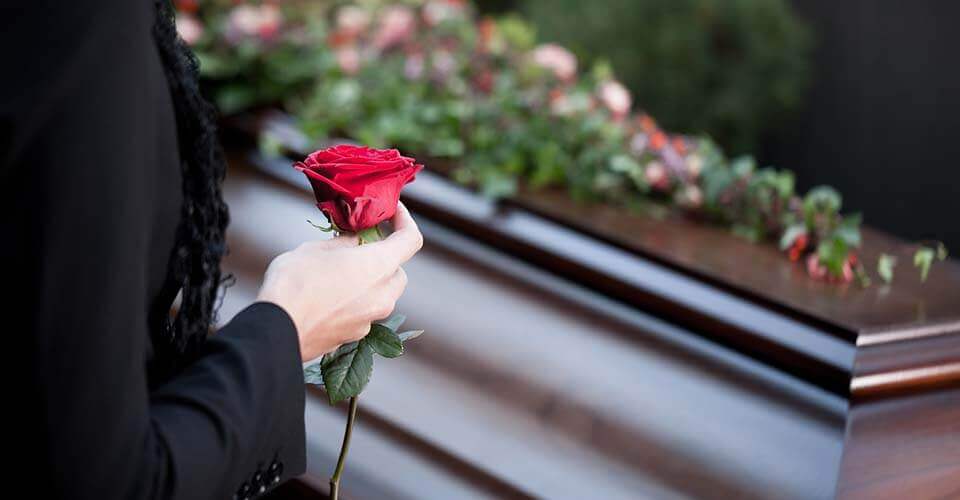 Person dressed in black holding a single rose standing in front of a casket