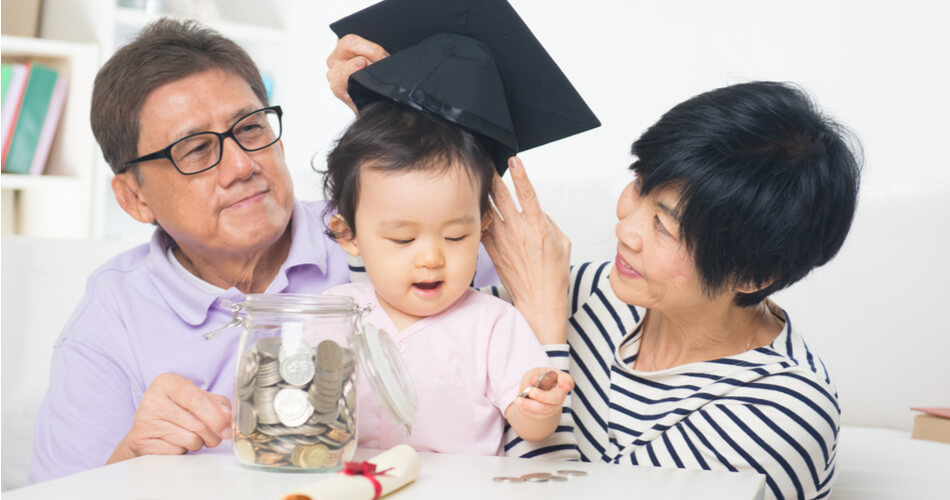 Family at a table putting a graduation cap on a toddler while the child plays with coins in a mason jar