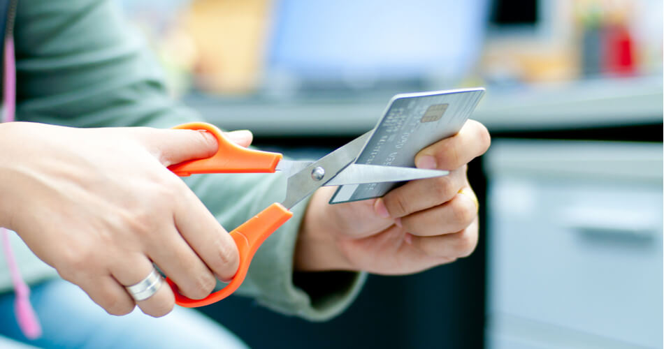 Person holding a metal credit card with a pair of scissors at the edge of the card