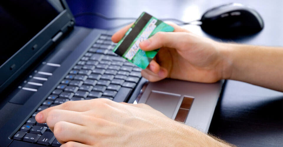 A man typing on a keyboard while holding a credit card in his other hand