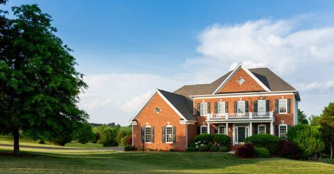 Large manor with an open yard next to a tall tree