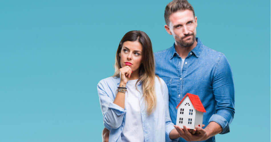 Woman looking questioningly to the side while man holds house model