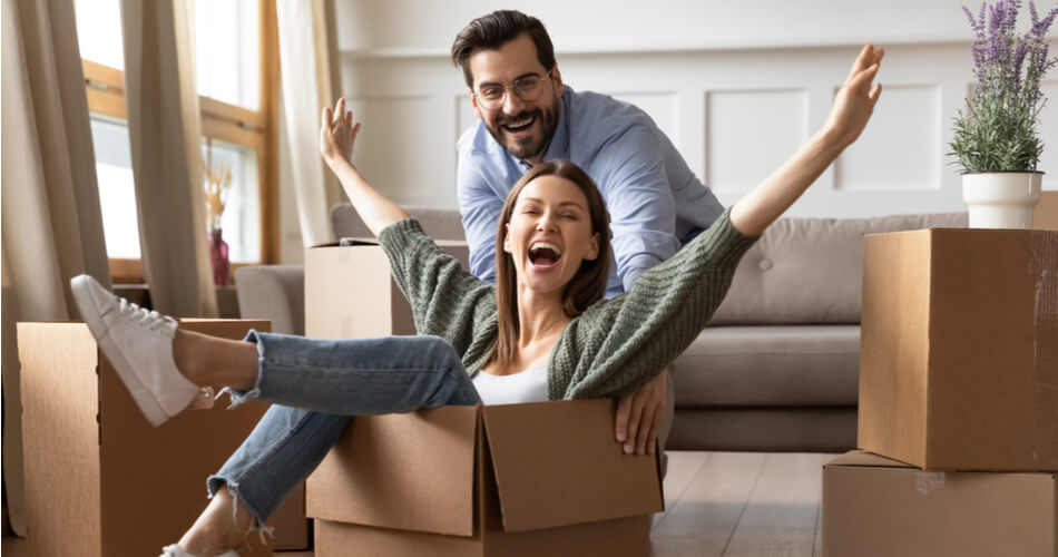 Young woman in her 20s a moving box with her arms up while a young man pushes her in the box