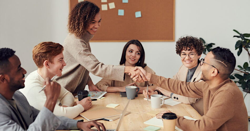 smiling employees around meeting table, two shaking hands