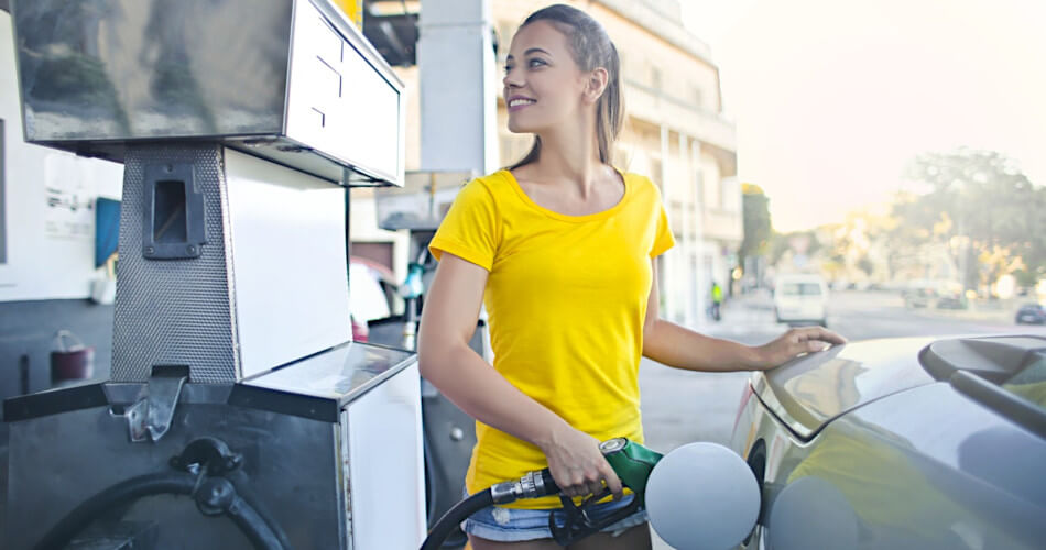 woman in yellow shirt fills her gas tank, smiling because she gets such good gas mileage