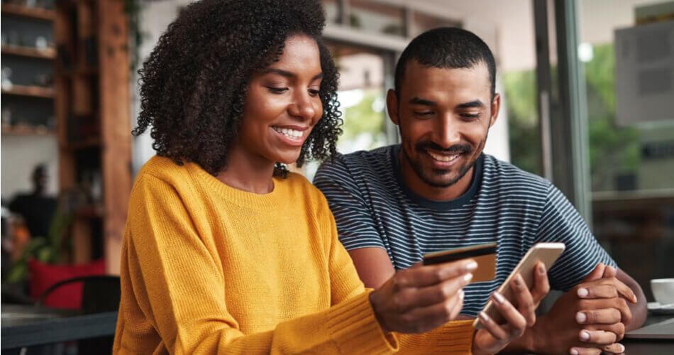 Couple smiling at a phone and holding a cashback debit card