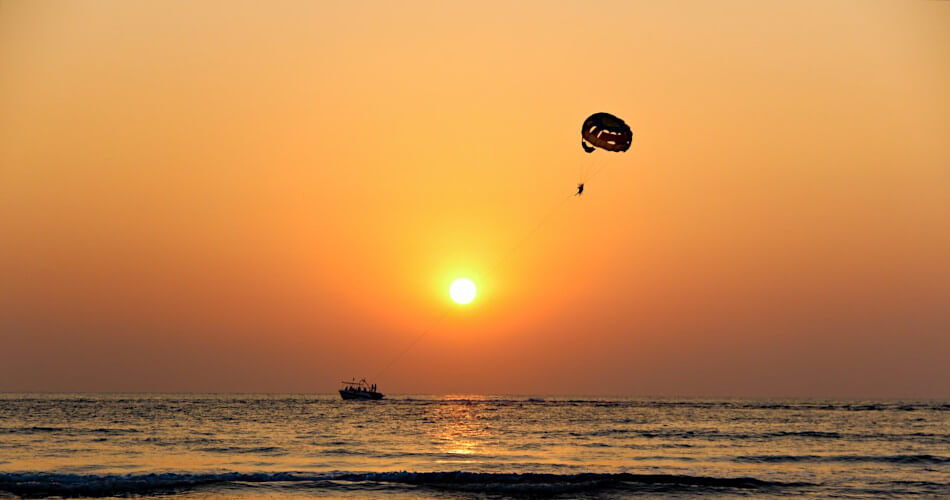 golden sun, orange sky, and parachute over water