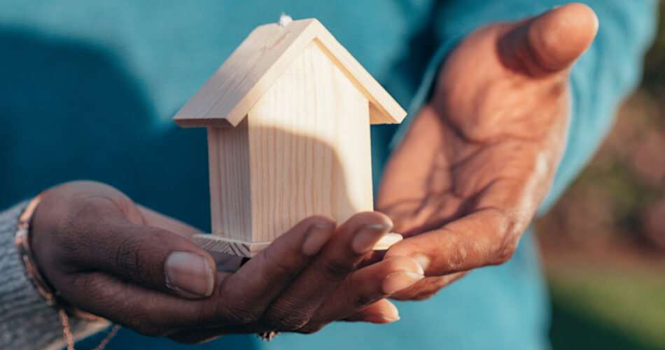 hands holding wooden model of house, symbolizing home ownership