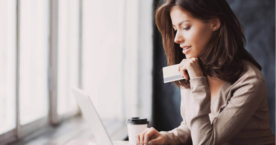 Woman holding a credit card and coffee cup looking at a laptop