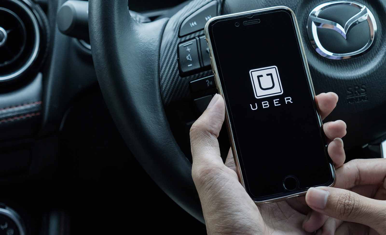 Hand holding a smartphone with the Uber logo in front of a steering wheel