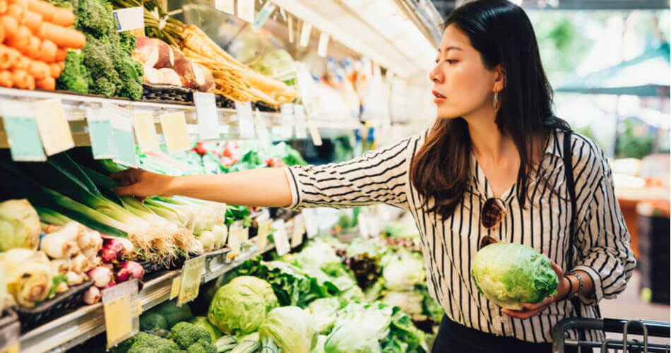 Woman holding a head of lettuce reaching for produce in a grocery store