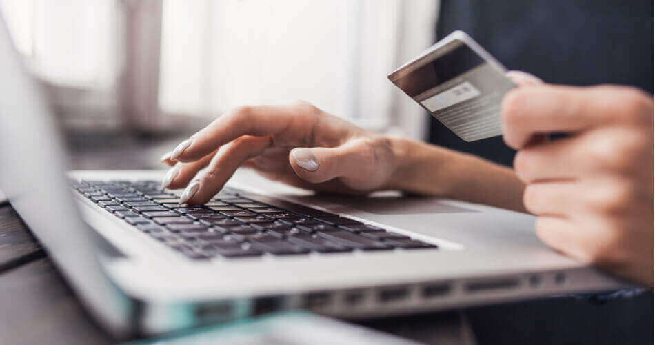 Hands typing on a laptop keyboard while holding a credit card