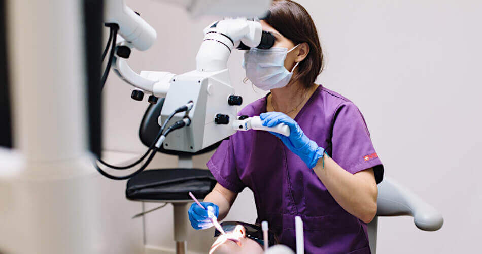 Dental assistant in scrubs taking a closer look at a patient's root canal