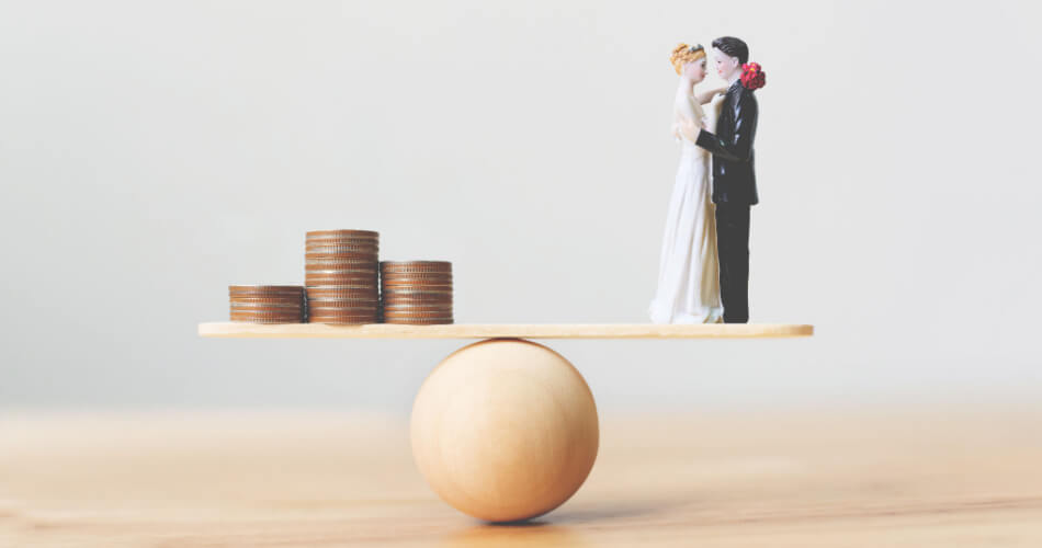 Stacks of coins and wedding figurines on opposite ends of a seesaw