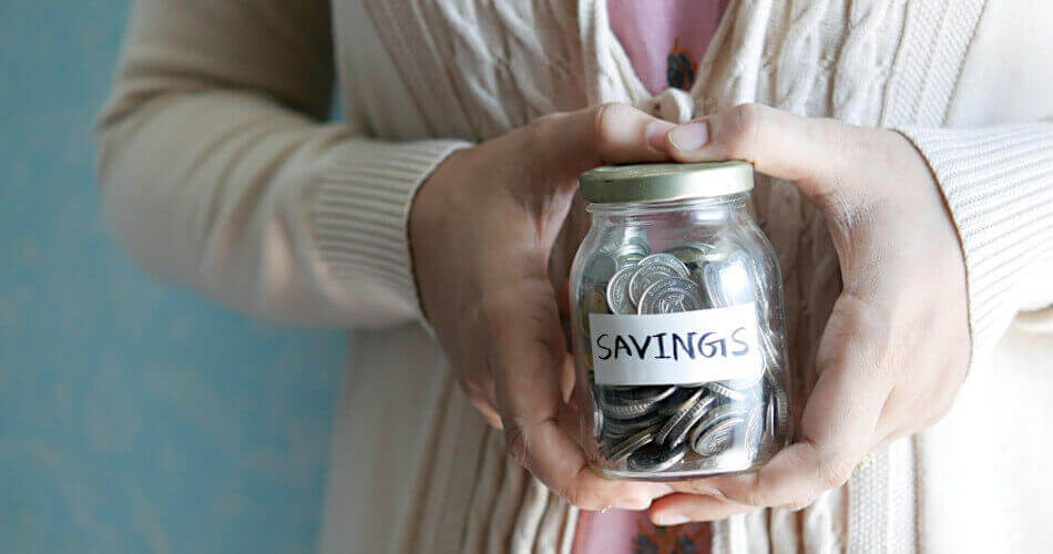 Hands holding a jar of coins labeled savings
