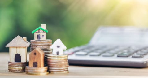 Small house models on top of coin stacks, representing the pros and cons of home equity loans and other equity financing