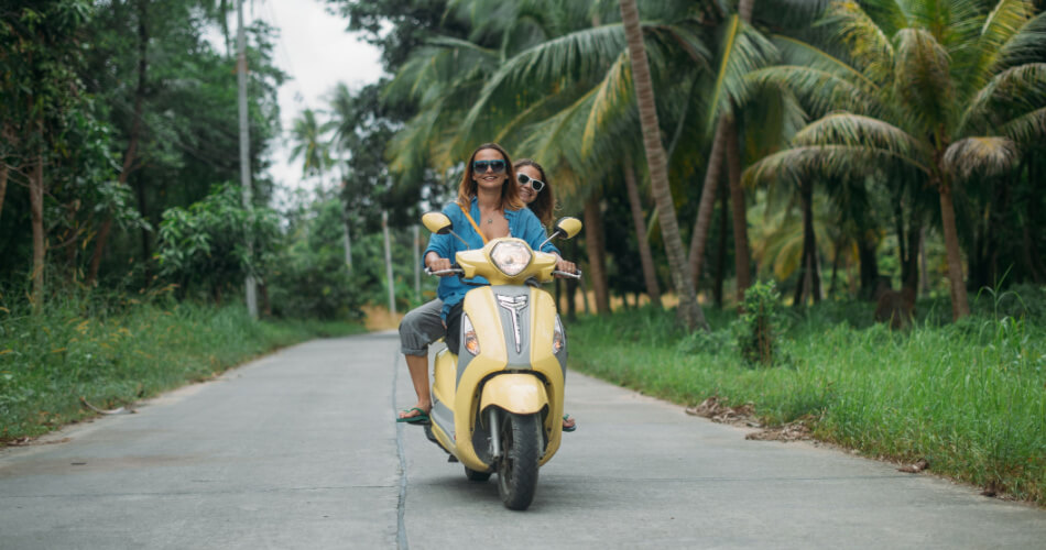 Two young women driving a moped through the jungle