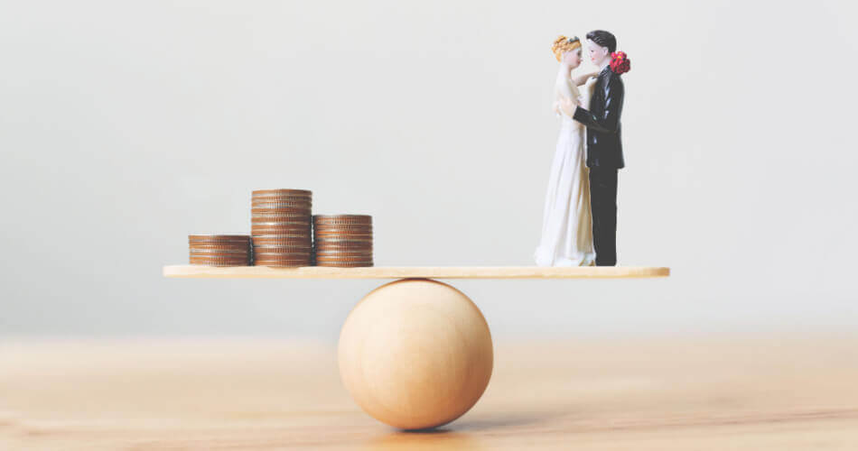 Stacks of coins and wedding figurines on opposite ends of a seesaw, representing the cost of a wedding and how many people you should invite to your wedding