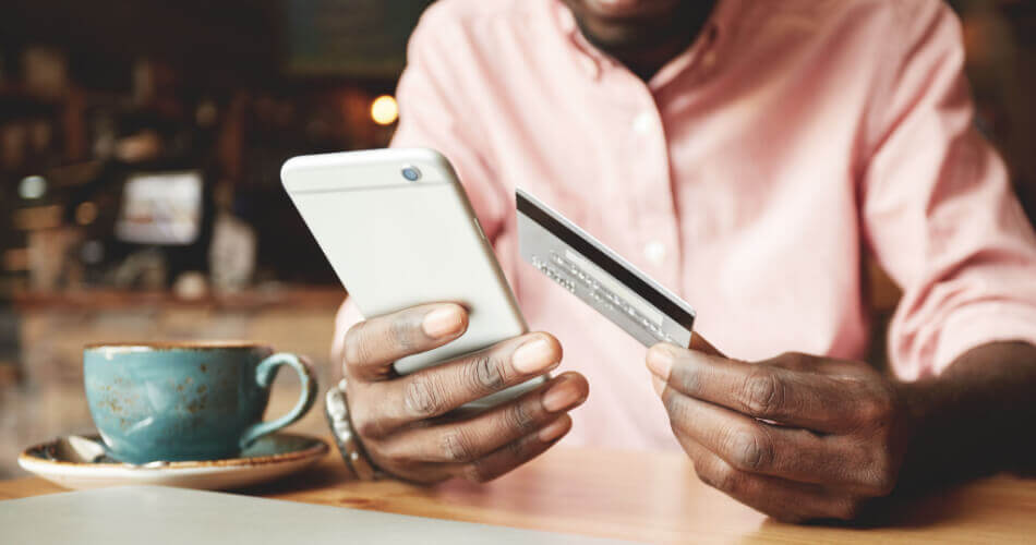 Man holding a credit card in one hand while looking at a smartphone in his other hand